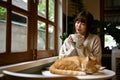 Relaxed young Asian woman sipping tea at a table with her orange cat Royalty Free Stock Photo