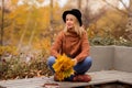 Relaxed young blonde in a brown warm sweater, black felt hat, blue jeans and boots sits on a bench in the autumn in the park, Royalty Free Stock Photo