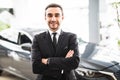 Relaxed young businessman or salesman with hands crossed in front of car