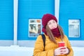 Relaxed young Caucasian woman with coffee in her hands in winter on the street against the background of a blue building