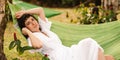 Relaxed young caucasian woman looking at camera lying in hammock in backyard of country house.