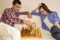 Relaxed young couple playing chess at home lying on sofa. won - Friendship.