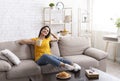 Relaxed millennial girl sitting on sofa with cup of coffee at home, enjoying peaceful morning