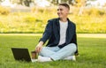 A relaxed young man sitting on the grass with a laptop and a coffee cup Royalty Free Stock Photo