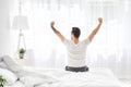 Relaxed young man waking up in bed and stretching his arms, facing the window, back view, free space Royalty Free Stock Photo