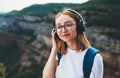 Relaxed young traveler woman hipster meditates with eyes closed listening to favorite music on wireless headphones while walking Royalty Free Stock Photo