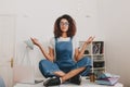 Relaxed young woman with bronze skin sitting in lotus pose on the table with laptop and documents. Indoor portrait of Royalty Free Stock Photo