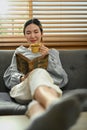 Relaxed young woman drinking hot coffee and reading book, spending free time in Sunday morning at home Royalty Free Stock Photo