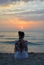 Relaxed young woman sits on a sun-drenched beach with her legs crossed, doing yoga