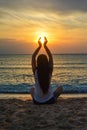 Relaxed young woman sits on a sun-drenched beach with her legs crossed, doing yoga