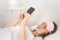 Relaxed young woman using a smartphone in the morning on the bed at home. Happy and smiling girl using a mobile phone Royalty Free Stock Photo