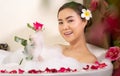 Relaxing beautiful Asian woman pampering her body in water in a spa bathtub with white foam bubble of soap and rose petals. Royalty Free Stock Photo