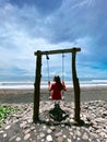 Relaxing day at Medewi beach, young girl in red dress on the swing, Bali, Indonesia. Black sand beach. Royalty Free Stock Photo
