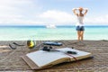 Relaxing girl, opened empty notepad is on the table with sunglasses, phone and headphones at the tropical sea background