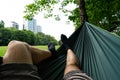 relaxing in the green hammock in the summer in a city park. Socks in feet close up. Buildings and grass background. Man legs Royalty Free Stock Photo