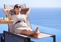 Relaxing while on holiday. A posh young woman reclining on a deck chair with her hands behind her head. Royalty Free Stock Photo