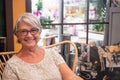 Relaxing moment for one smiling senior pretty lady with gray hair looking at camera. Romantic and rustic corner. Window in