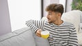 Relaxing morning, handsome young arabian man with a beard, comfortably resting on his sofa at home, enjoying his cup of espresso, Royalty Free Stock Photo