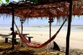 Rustic tent on the beach covered by vegetal dry keaves. Red hammock waiting for relaxing Royalty Free Stock Photo