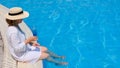 relaxing senior woman dangling her legs in an outdoor swimming pool holding a blue refreshing cocktail wearing a straw Royalty Free Stock Photo