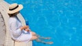 relaxing senior woman dangling her legs in an outdoor swimming pool holding a blue refreshing cocktail wearing a straw Royalty Free Stock Photo