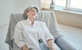 Relaxing smiling senior woman sitting on a cozy chair, stretching, relaxing, Royalty Free Stock Photo