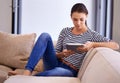 Relaxing with some time online. A beautiful young woman using a tablet on her couch. Royalty Free Stock Photo