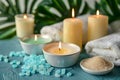 Relaxing Spa Setting with Lit Candles, Towels, Bath Salts, and Green Tropical Leaves on Teal Background for Wellness and Royalty Free Stock Photo