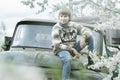 Relaxing teenager wearing woolly hand-knitted reindeer sweater sitting outdoors on old truck body at blooming fruit garden backgro Royalty Free Stock Photo