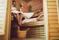 Relaxing teens couple wrapped white sheets lying and sweating on wooden bench in Hot Finnish sauna enjoying pleasant body care