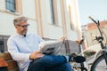 Relaxing time in city. man reading newspaper in city , bicycle in blurred background Royalty Free Stock Photo