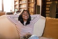 Cheerful young black woman resting on cozy couch with closed eyes, holding hands behind her head, napping at home Royalty Free Stock Photo