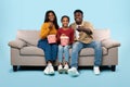 Relaxing together. Happy african american family watching television, parents sitting with their daughter on sofa Royalty Free Stock Photo