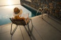 Relaxing vacation - woman sitting in chair and reading a book on terrace near swimming pool at luxury villa Royalty Free Stock Photo