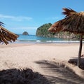 Relaxing in view of the sea, under the shadow of the palm trees, the sand bathed by the waves and rocky formations on the horizon Royalty Free Stock Photo