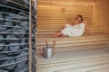 Relaxing Woman wrapped white towel lying and sweating on the wooden bench in Hot Finnish sauna with hot stones and enjoying Royalty Free Stock Photo