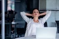 Relaxing at working place. Attractive young woman holding hands behind head and keeping eyes closed while sitting at her Royalty Free Stock Photo