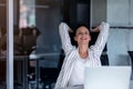 Relaxing at working place. Attractive young woman holding hands behind head and keeping eyes closed while sitting at her Royalty Free Stock Photo