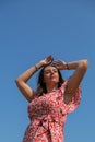 Relaxing young millennial woman in red dress against blue sky. Beautiful smiling girl on summer having fun. Enjoying sun Royalty Free Stock Photo