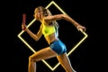 Relay exchange. Young female runner in action on black background with luminescent cube. Abstract desing, concept of