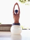 Releasing tension. A rear view shot of a muscular young man stretching while sitting on an exercise ball. Royalty Free Stock Photo