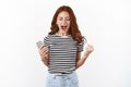 Relieved and happy excited young redhead woman in striped t-shirt, shouting yes, achieve victory, finally bit hard level