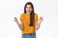 Relieved, happy woman rejoicing in yellow t-shirt, clench fists and smiling joyfully, achieve success, got lucky winning