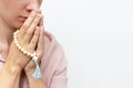 Religeous caucasian young woman praying and holding rosary in hands on white background, copy space