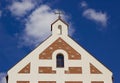 Religion symbol. Beautiful church with cross and red tile roof against a bright blue sky with flying birds and fluffy clouds. Royalty Free Stock Photo