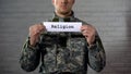 Religion word written on sign in hands of male soldier, faith in God, prayer