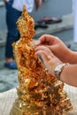 Religious ceremony at Buddhist temple. A woman sticking golden leaflets on a Buddha figurine.