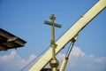 A religious cross and an arrow of a crane next to the roof of a church under construction against a background of blue sky and