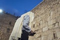 A religious Jewish man wearing traditional garment while reading prayer book at the background of the Wailing Wall in Royalty Free Stock Photo