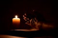 Book, candle and hands. Woman prays in dark. Reading prayers at night. Royalty Free Stock Photo